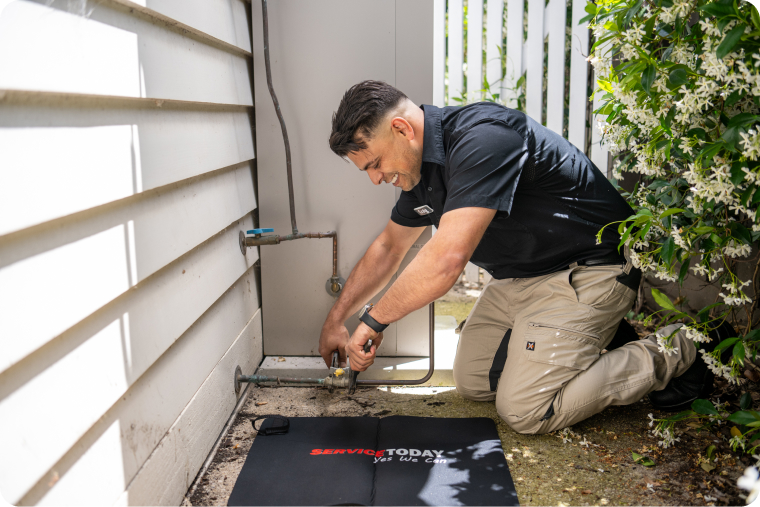 Plumber fixing a pipe leak outdoors for Service Today, emphasizing leak detection services.