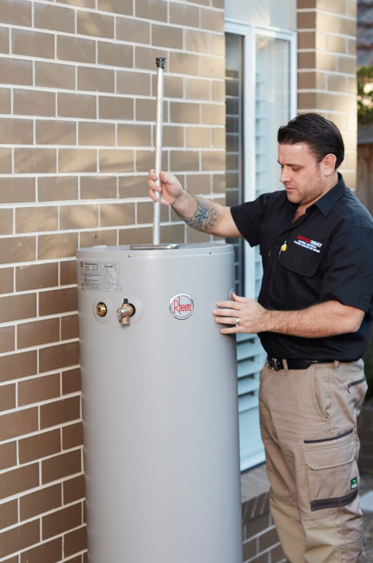 Plumber inspecting a Rheem hot water system outside a brick house.