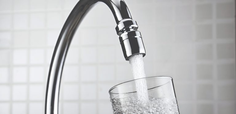 Water pouring from a faucet into a clear glass, filling it with bubbles.