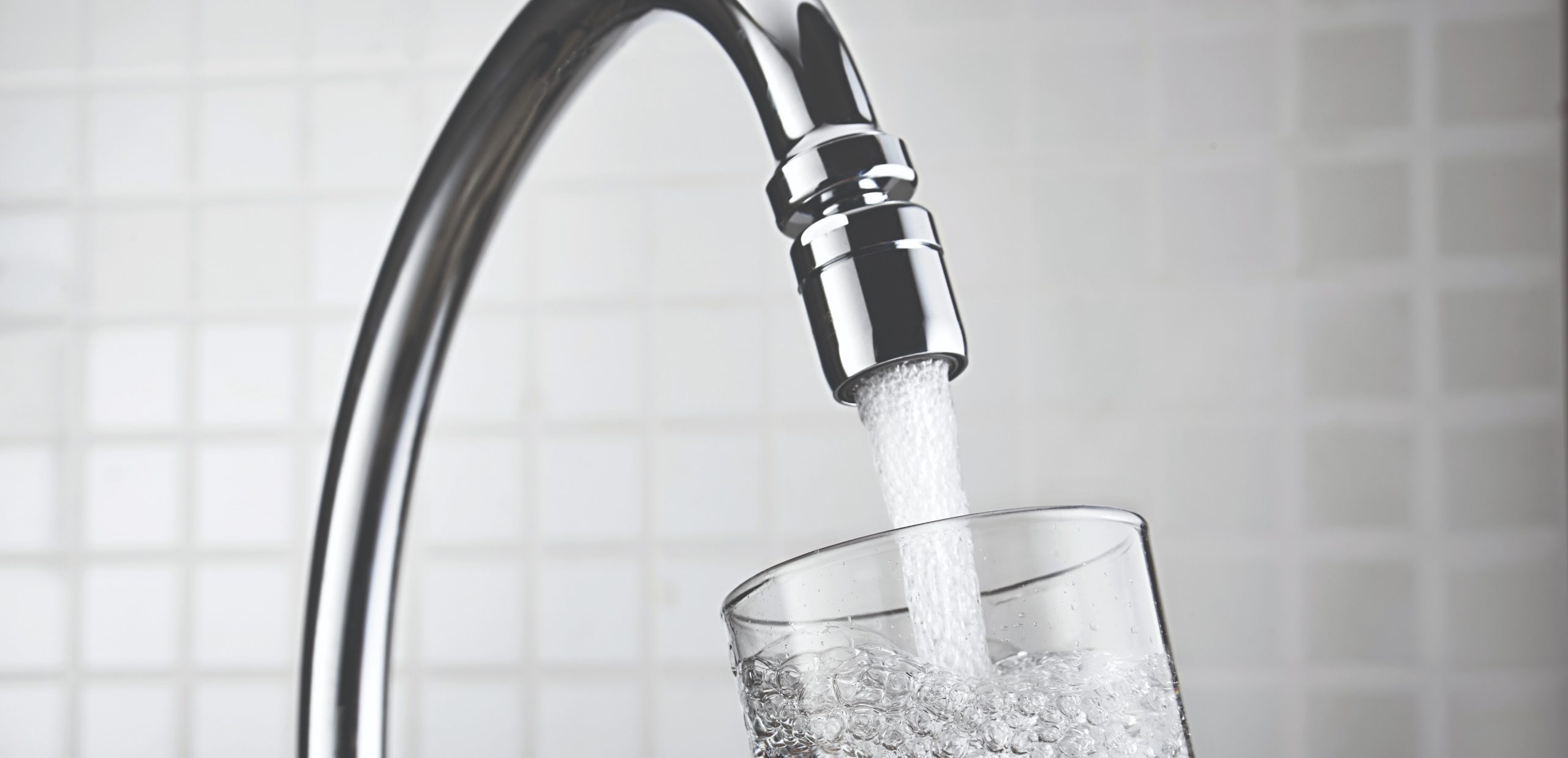 Water pouring from a faucet into a clear glass, filling it with bubbles.