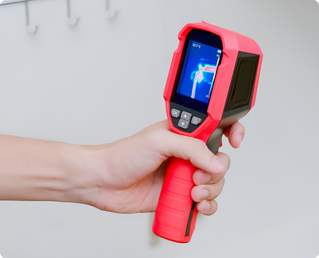 Hand holding a red thermal imaging camera to detect a leak.