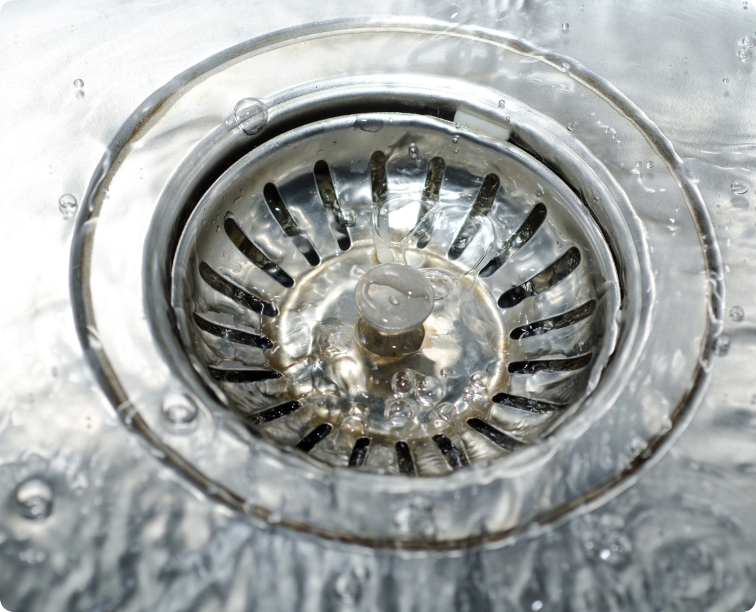 Close-up of water flowing into a clogged sink drain with a strainer.