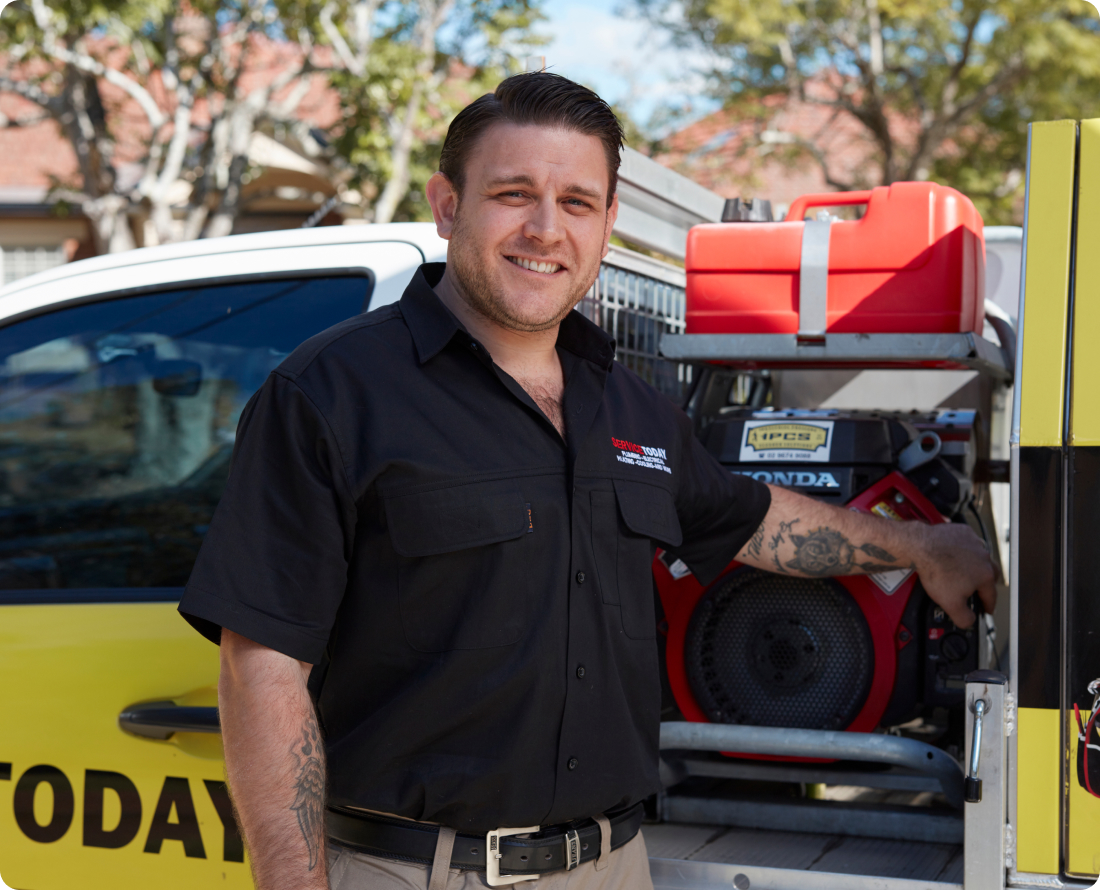 A man smiles in front of a service vehicle with equipment for plumbing services.