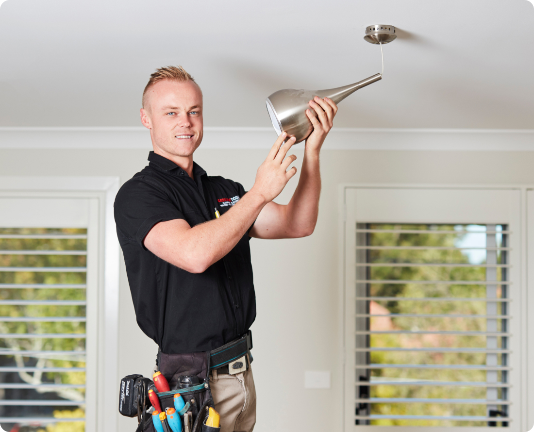Electrician installing a modern pendant light fixture on a white ceiling.