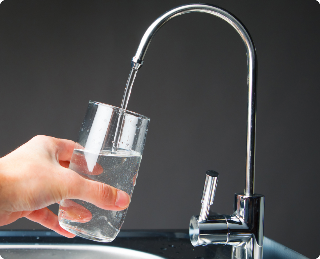 A hand holds a glass of water under a faucet filling with water.