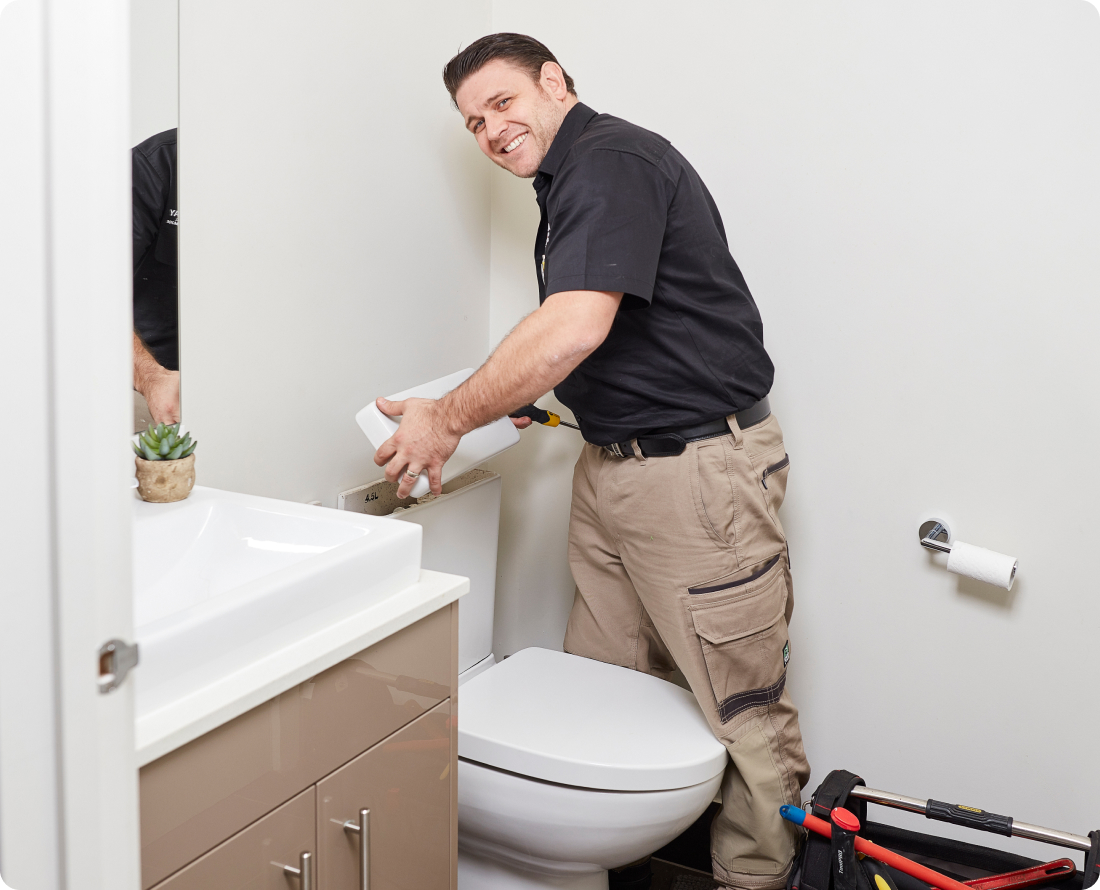 Plumber installing a toilet tank lid in a bathroom.