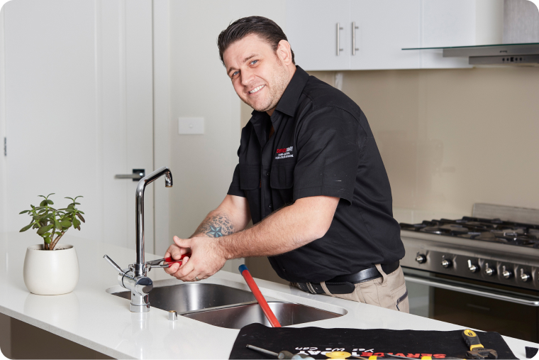 Plumber fixing a kitchen sink faucet with a wrench.