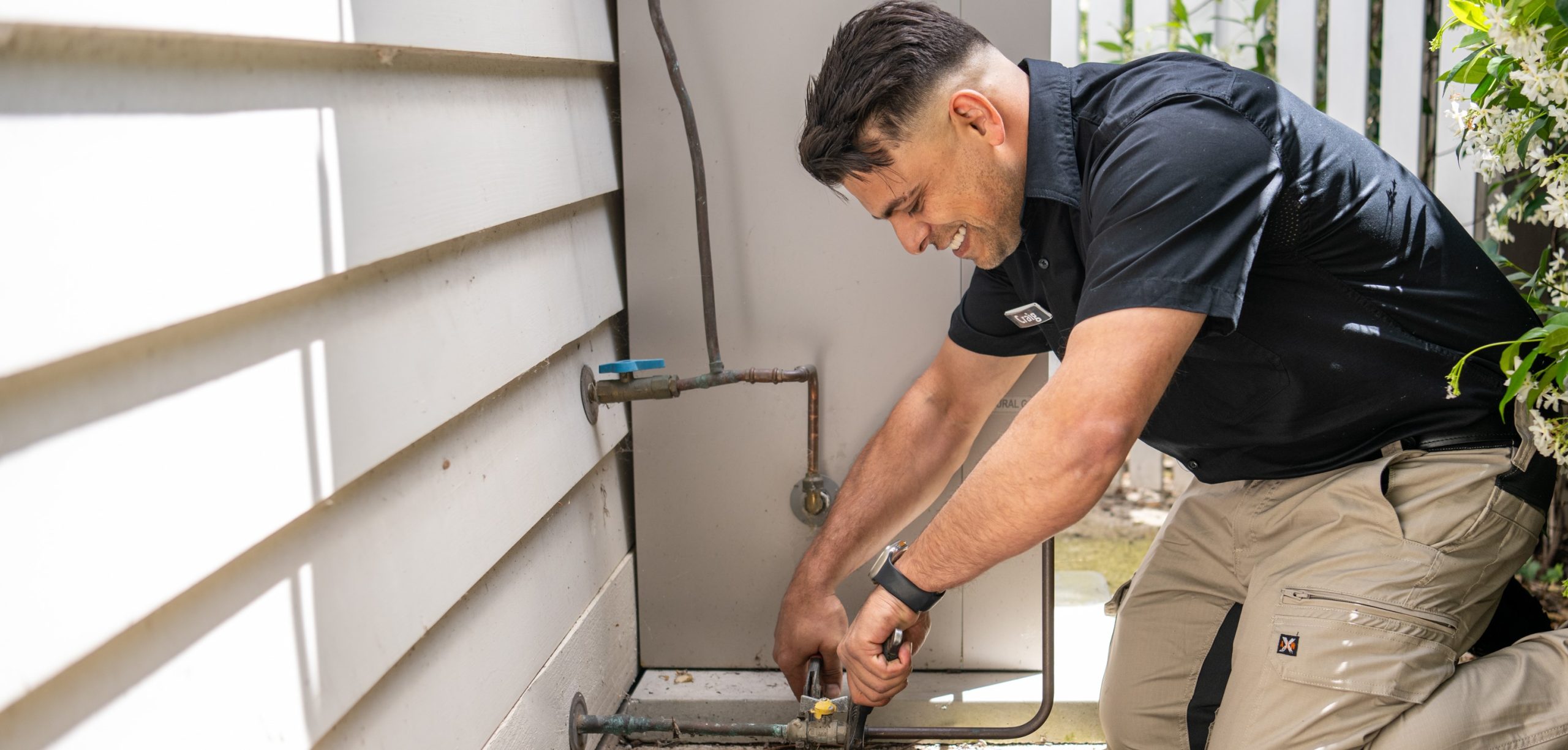 Plumber working on exterior gas line with tools.