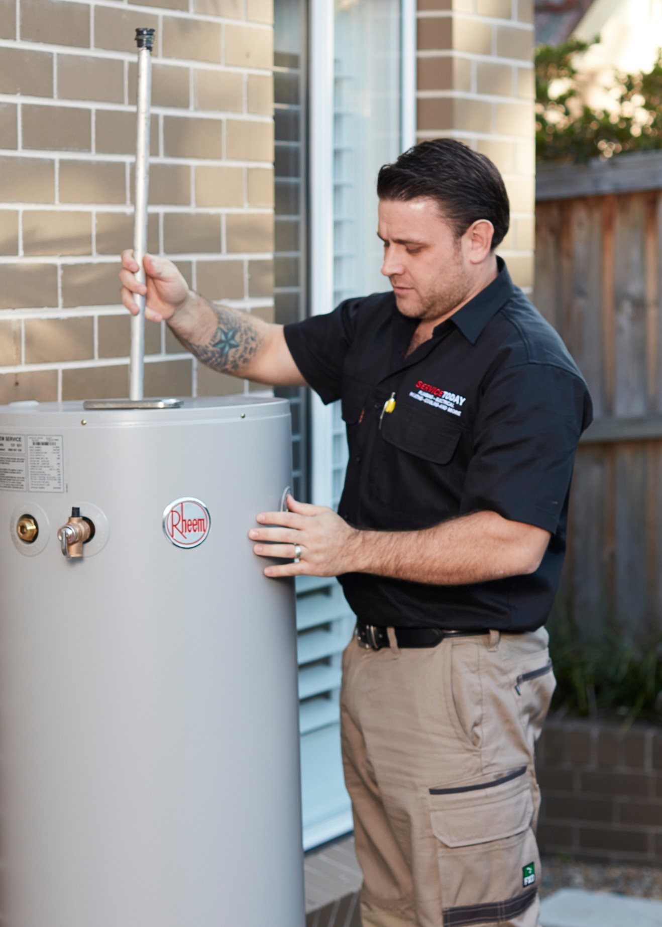 Plumber servicing a Rheem hot water system outside a house.