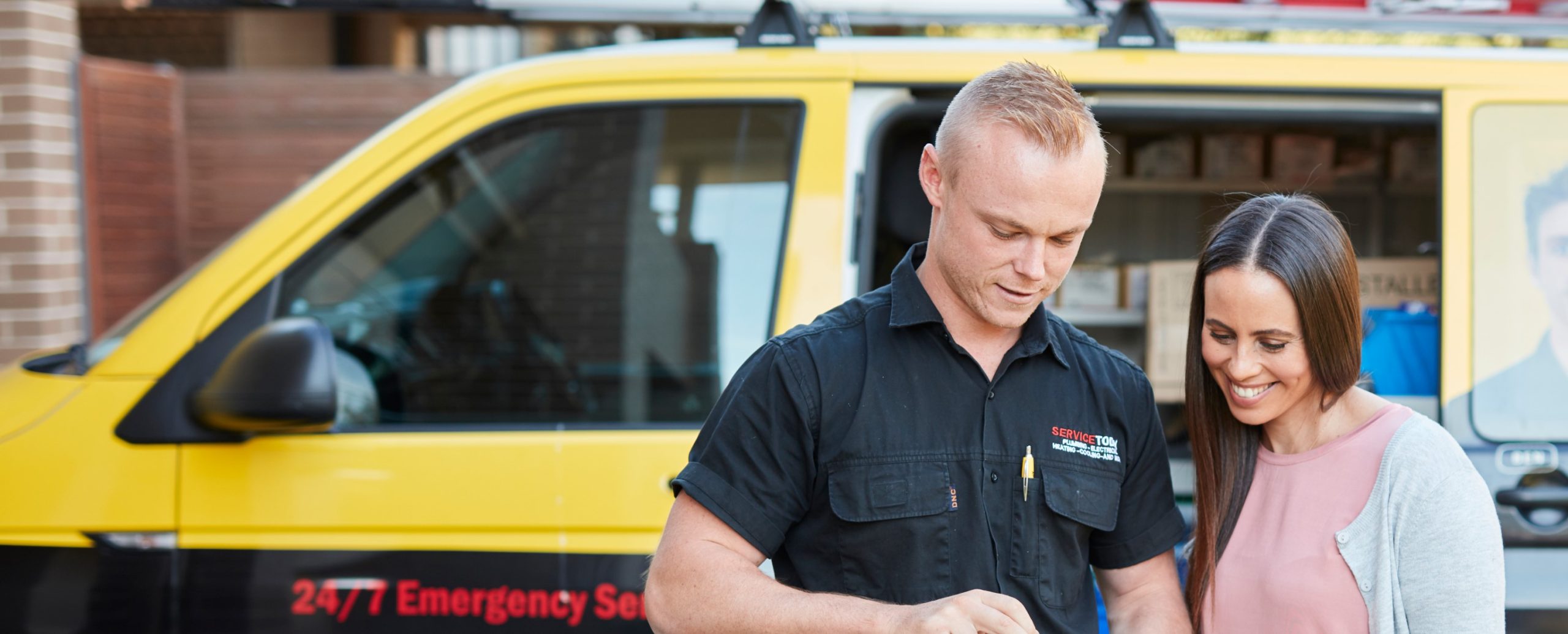 Technician discusses service with a customer outside a yellow service van.