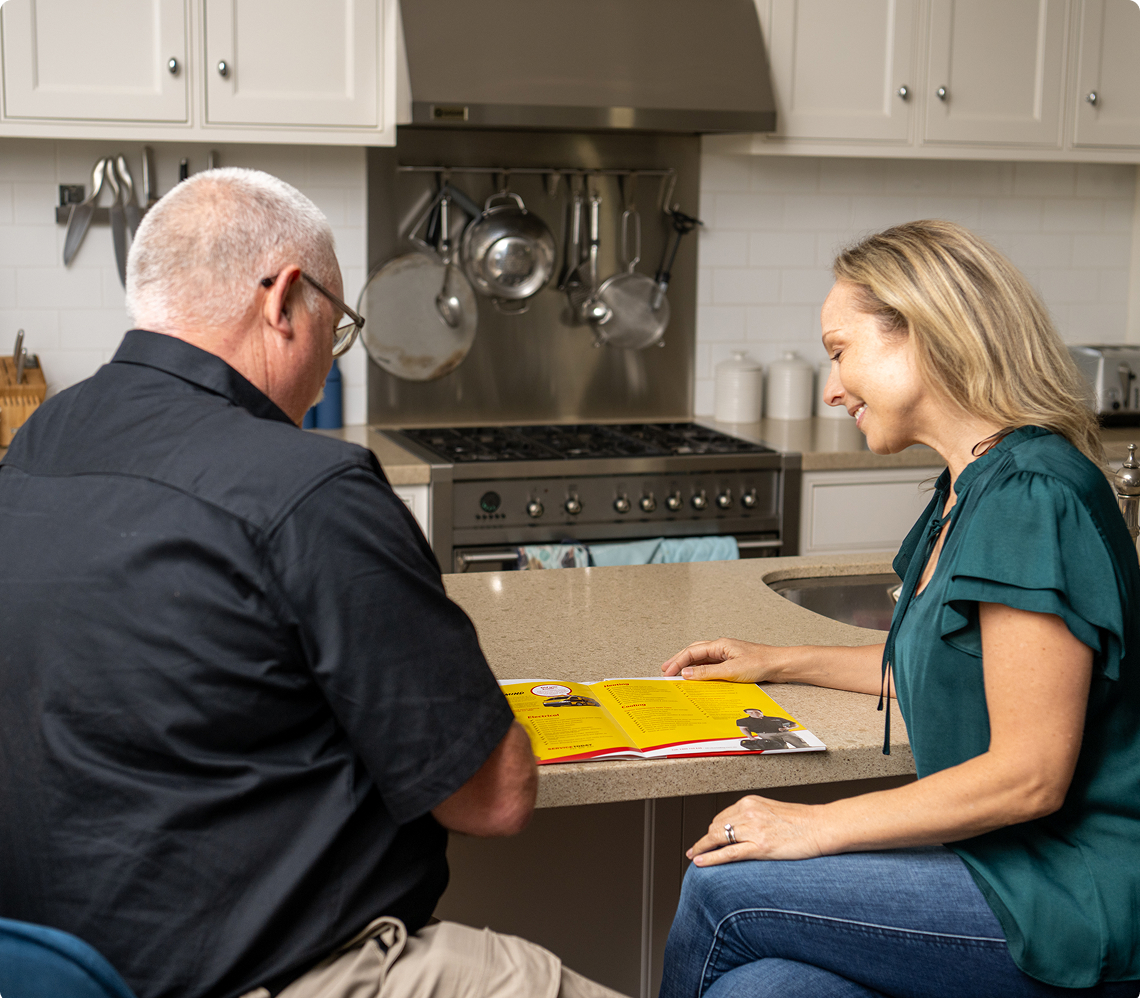 Couple reviews the Total Care Club booklet in a modern kitchen, discussing services.