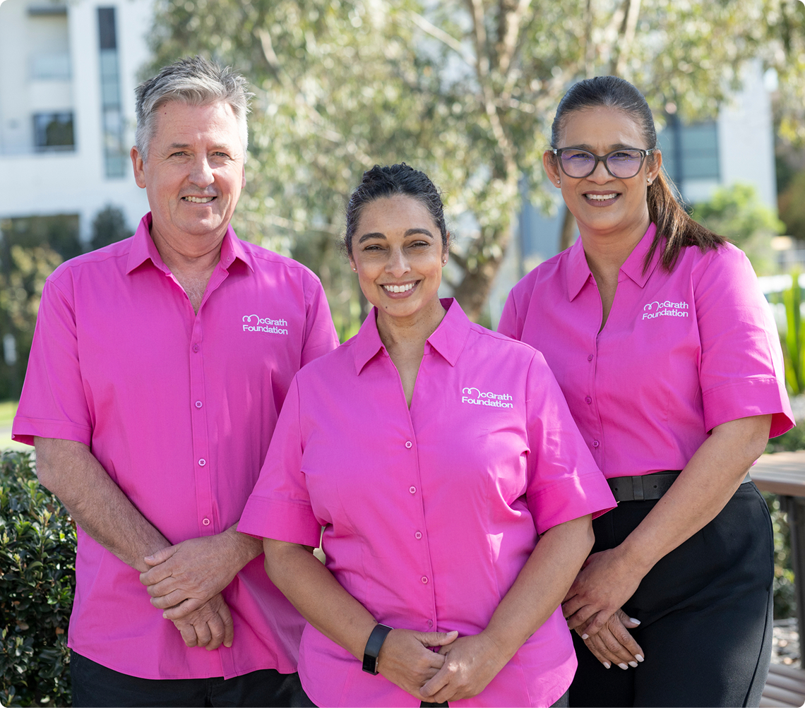 Three people in pink McGrath Foundation shirts smile for a photo outdoors.