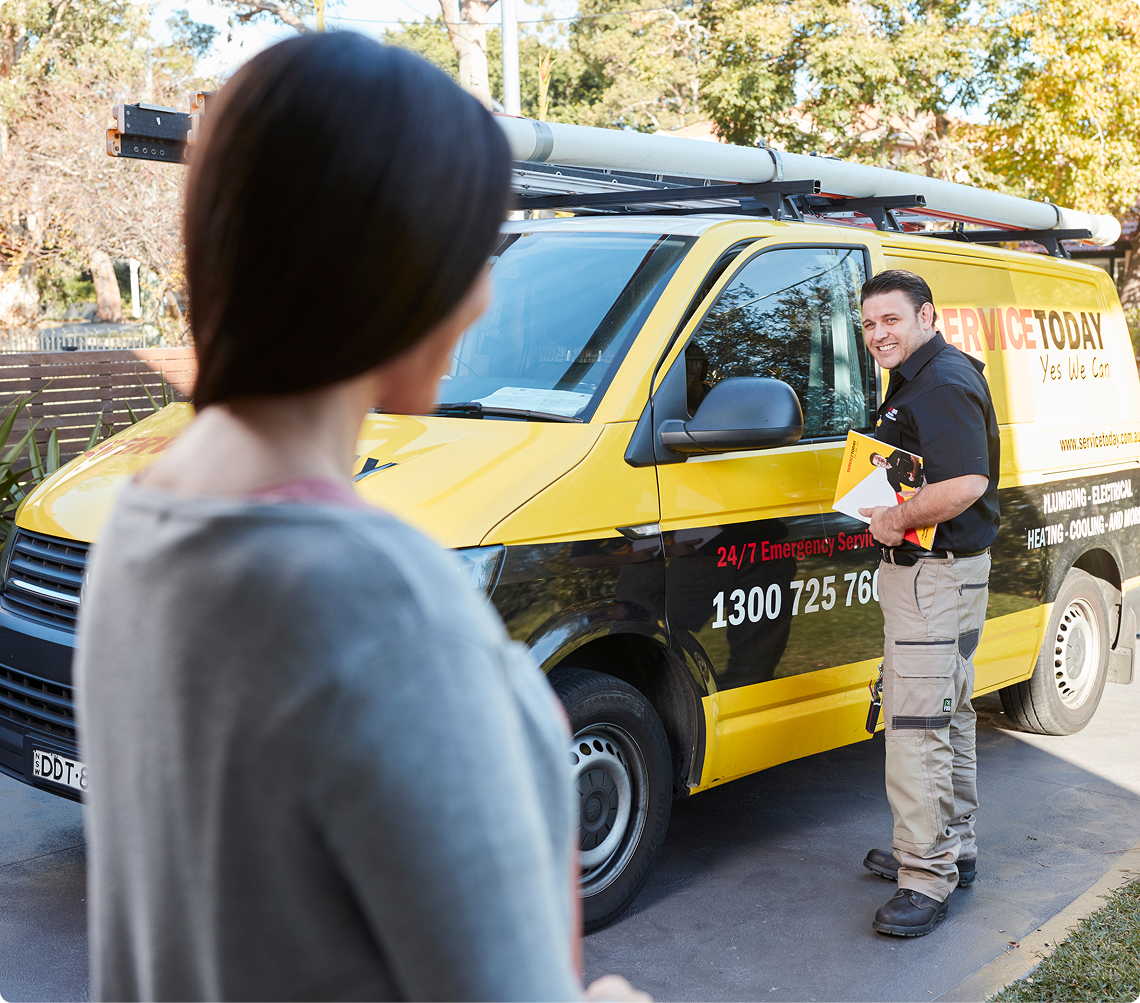 Plumber from Service Today smiles and holds brochure next to his van.