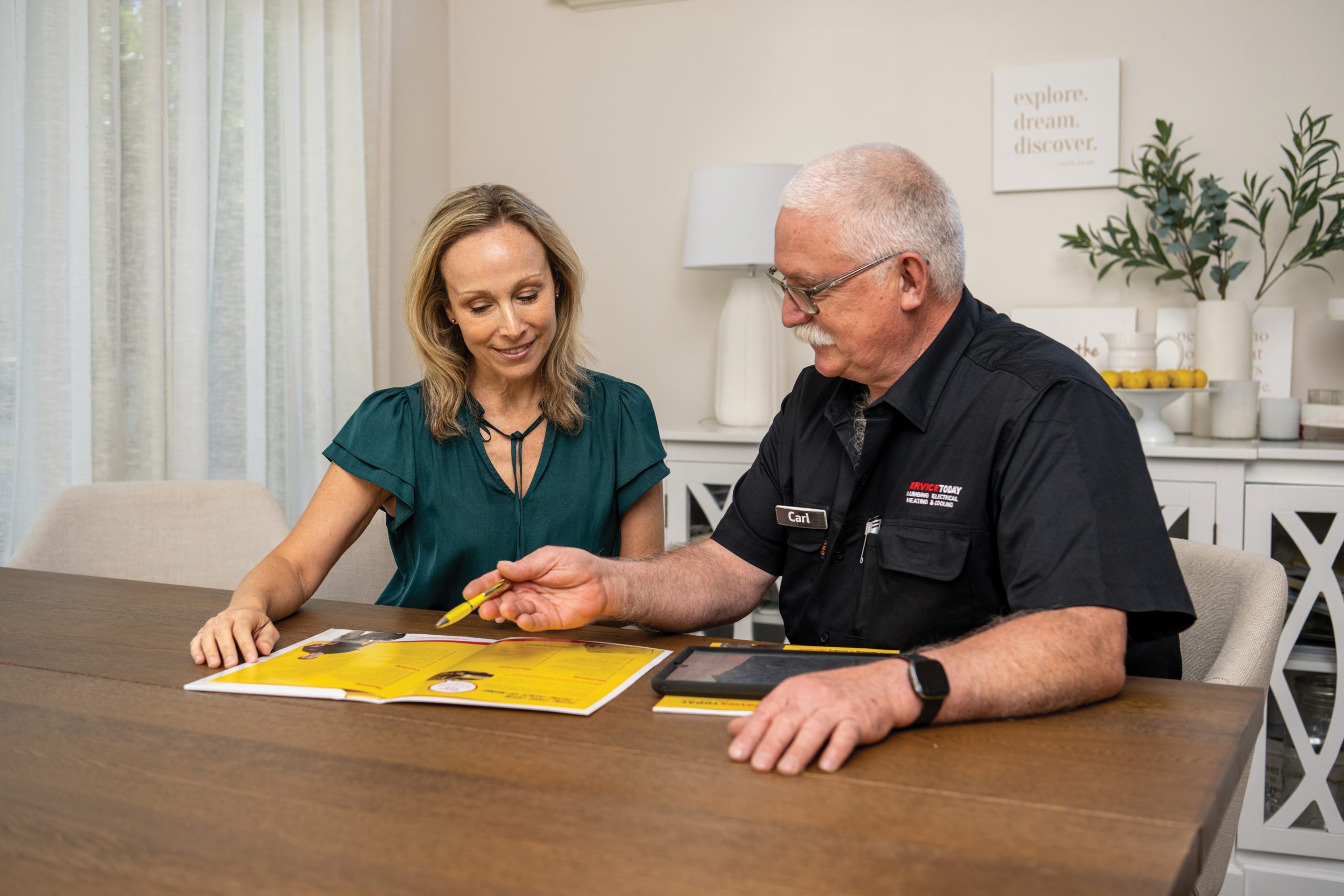 Man in a black uniform with "Carl" and "Service Today" on it points to a brochure with a woman.