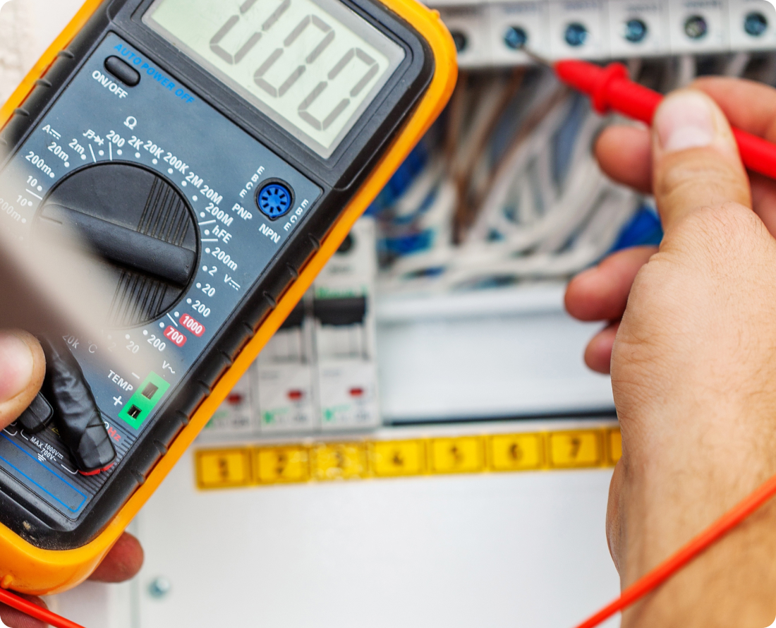 Close-up of a hand using a multimeter to test electrical wires in a control panel.