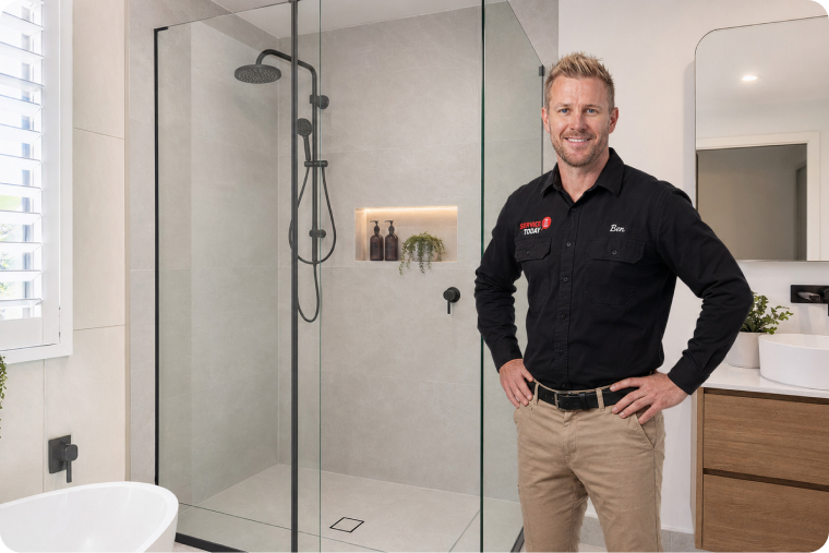 Ben from Service Today stands in a modern bathroom with a frameless glass shower.