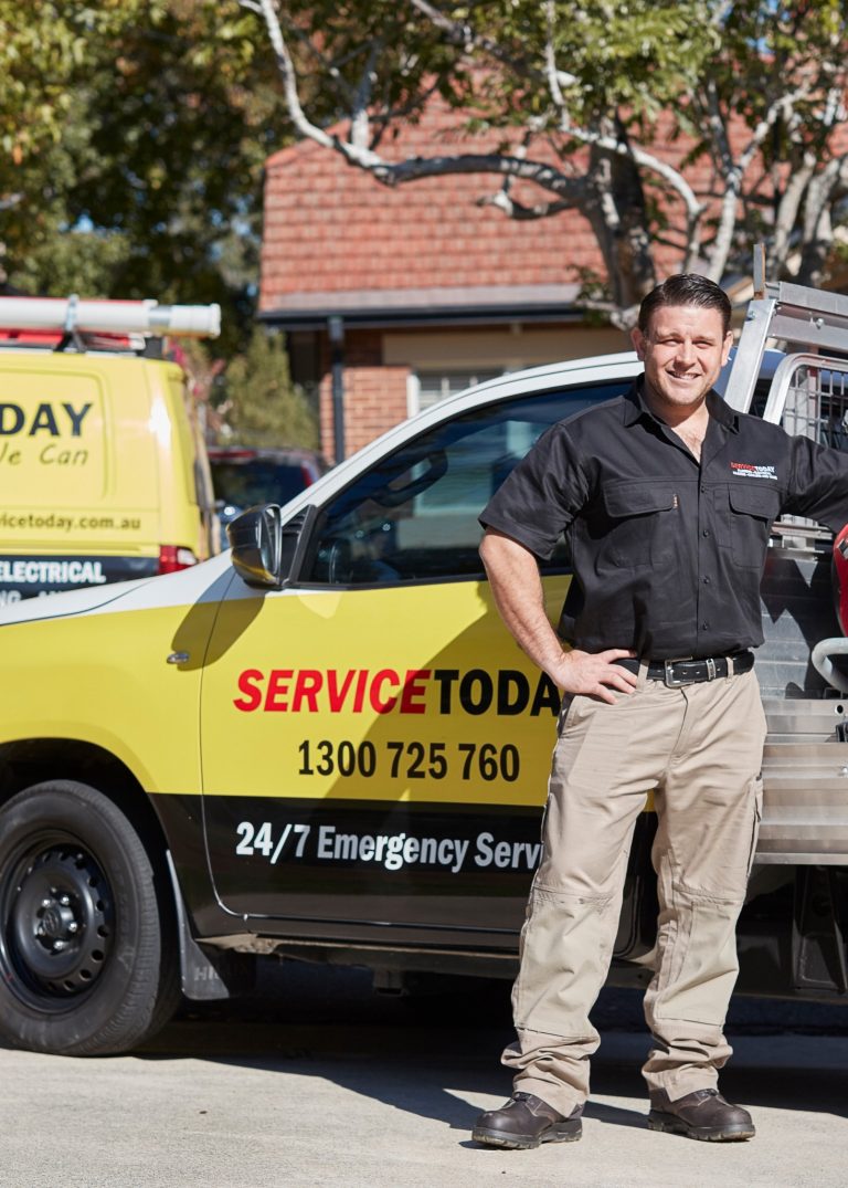 Tradesman in uniform standing by service vehicle with company branding and phone number.