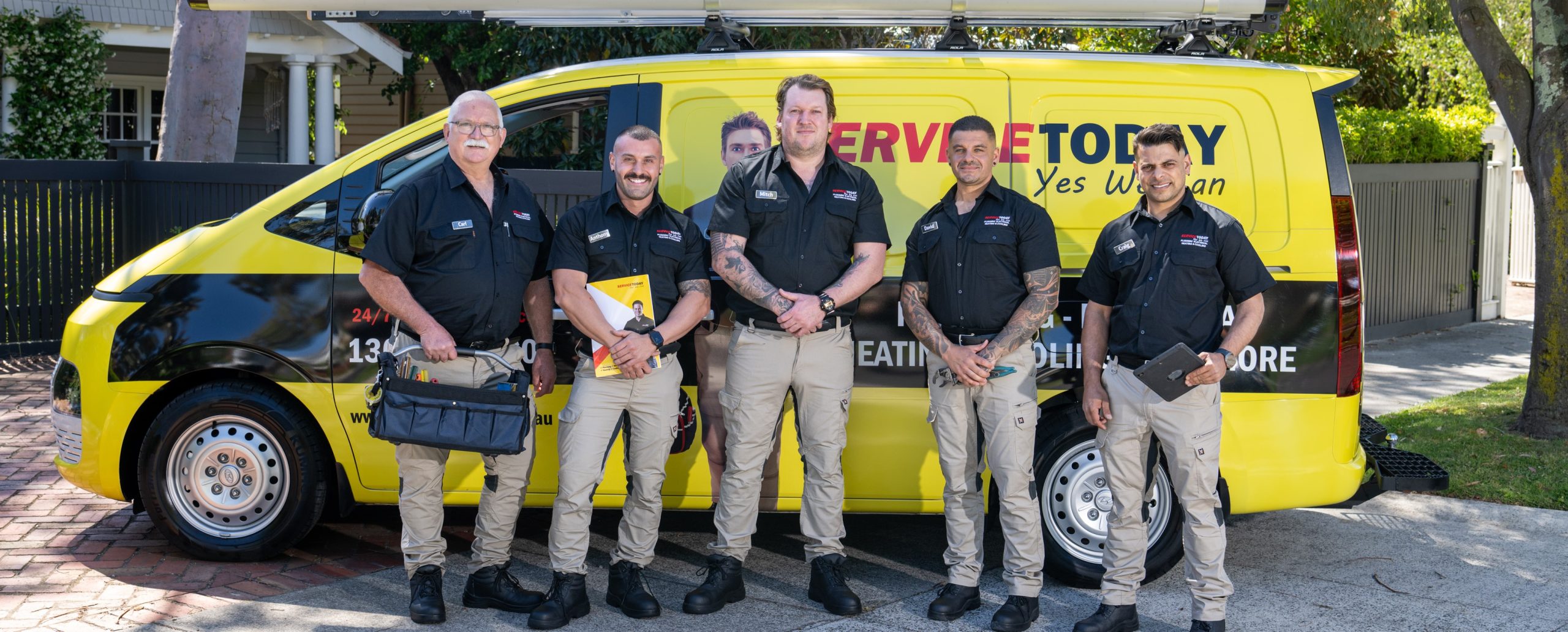 Service Today team of tradesmen, in uniform, standing in front of their branded yellow van.