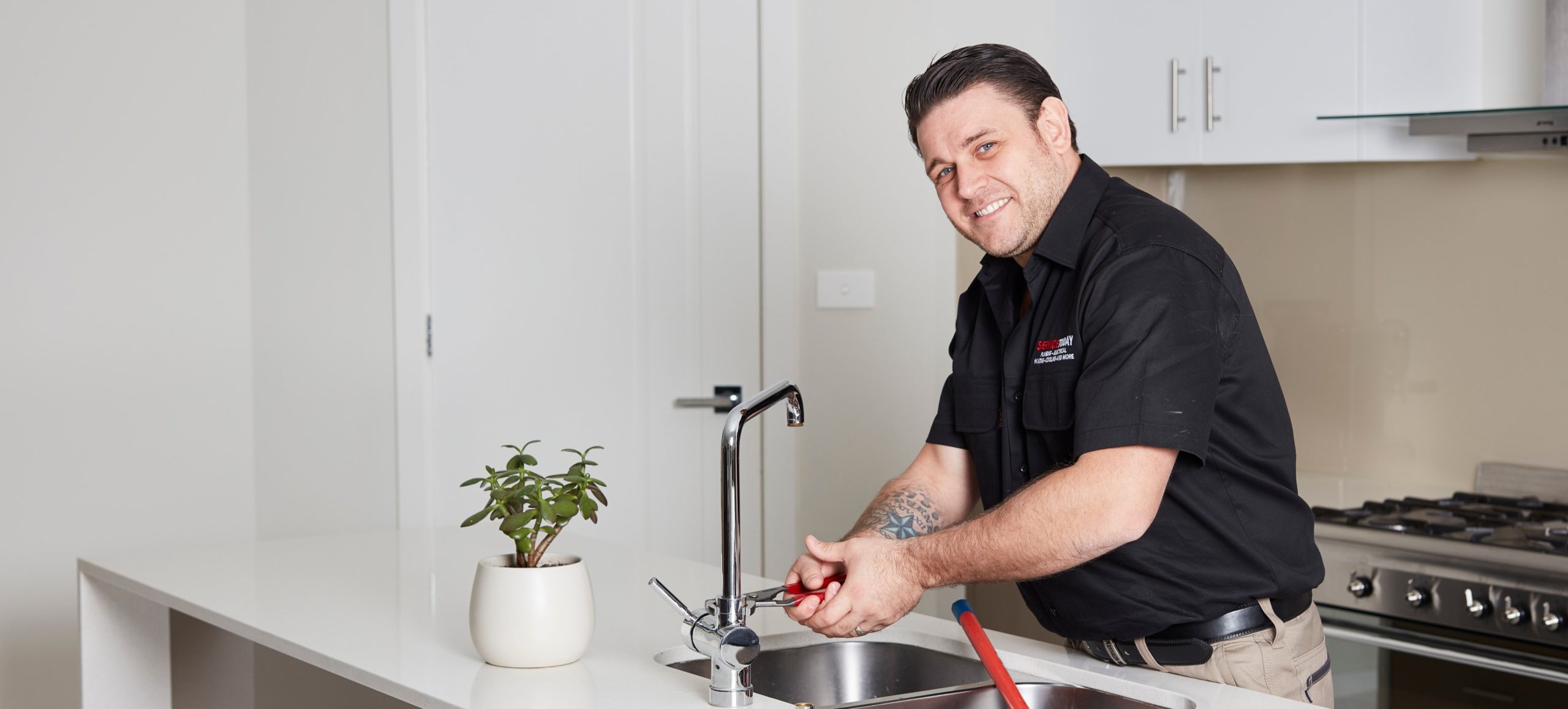 Plumber fixing a kitchen tap with a wrench.